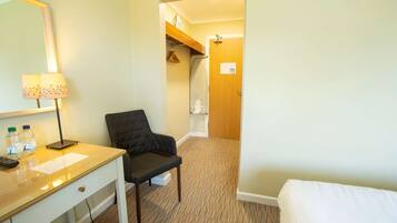 Une chambre d’hôtel équipée d’un bureau, d’une chaise, d’un lit et d’une salle de bain visible à travers une porte ouverte.