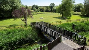 A wooden bridge over a stream with a picnic table and benches in a grassy park area.