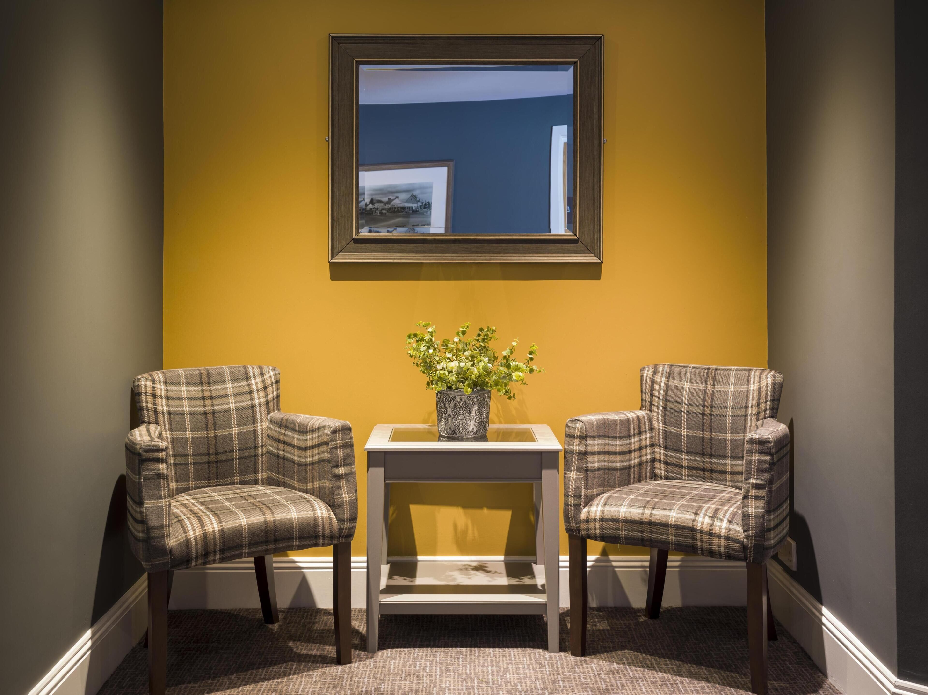 A room with two plaid chairs, a small table with a plant, and a framed picture on the wall.