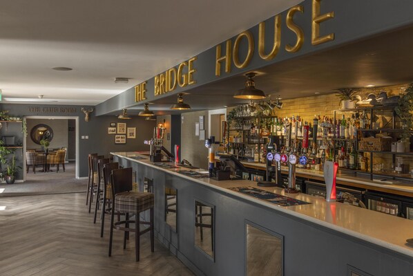 A bar area with a counter, bar stools, and a variety of bottles and glasses. - The Bridge House, BW Signature Collection (Ferndown)