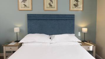 Una cama bien tendida con ropa de cama blanca, dos mesitas de noche con lámparas, y tres ilustraciones enmarcadas de pájaros en la pared.