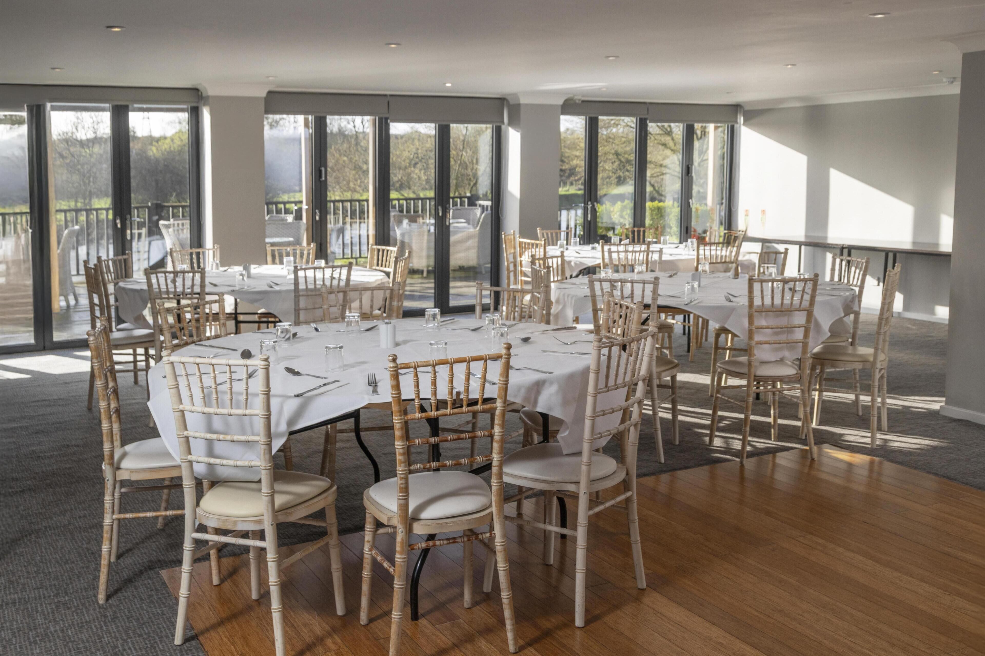 Un vaste espace dédié à la salle à manger, avec des tables rondes, des nappes blanches et des chaises en bois.