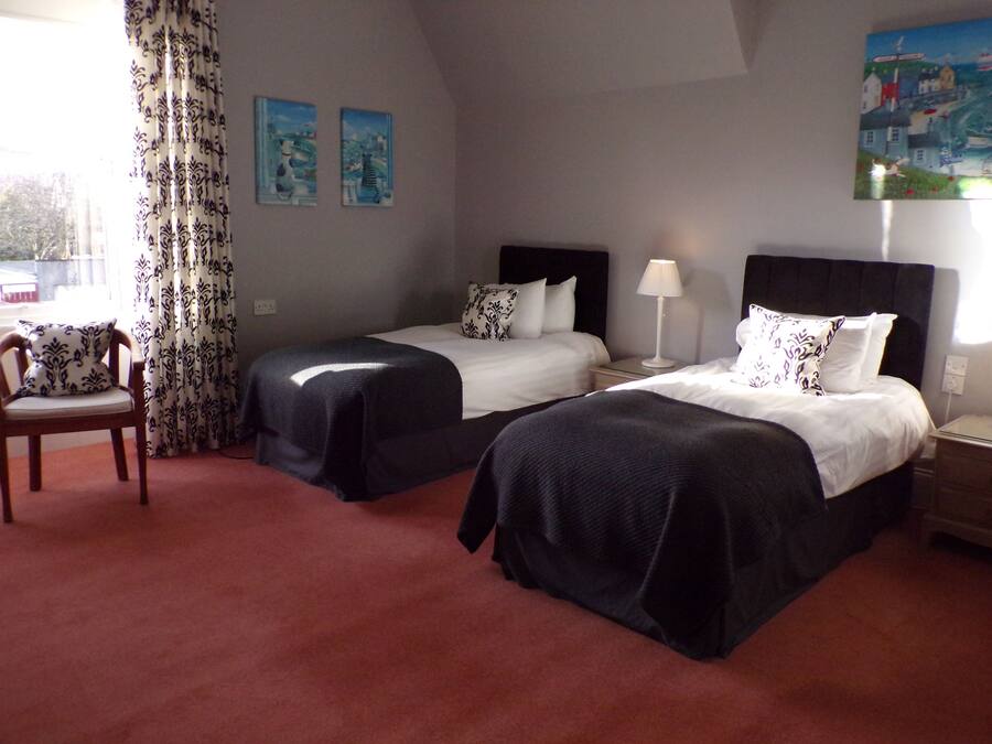 A hotel room with two beds, a chair, a lamp, and two paintings on the wall.