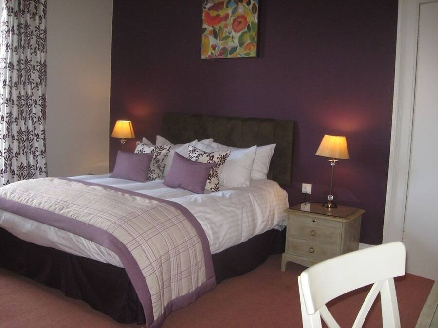 A bedroom with a bed, two bedside tables with lamps, a chair, and a floral painting on the wall.