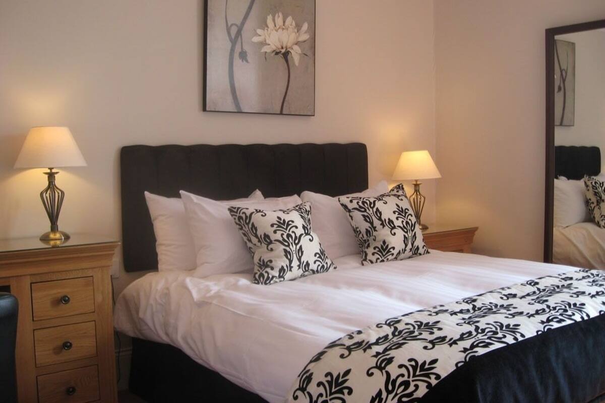 A neatly made bed with a dark headboard, two bedside lamps, and a floral painting above it.