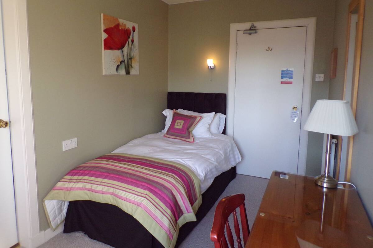 A bedroom with a bed, a bedside table, a lamp, a chair, and a door.