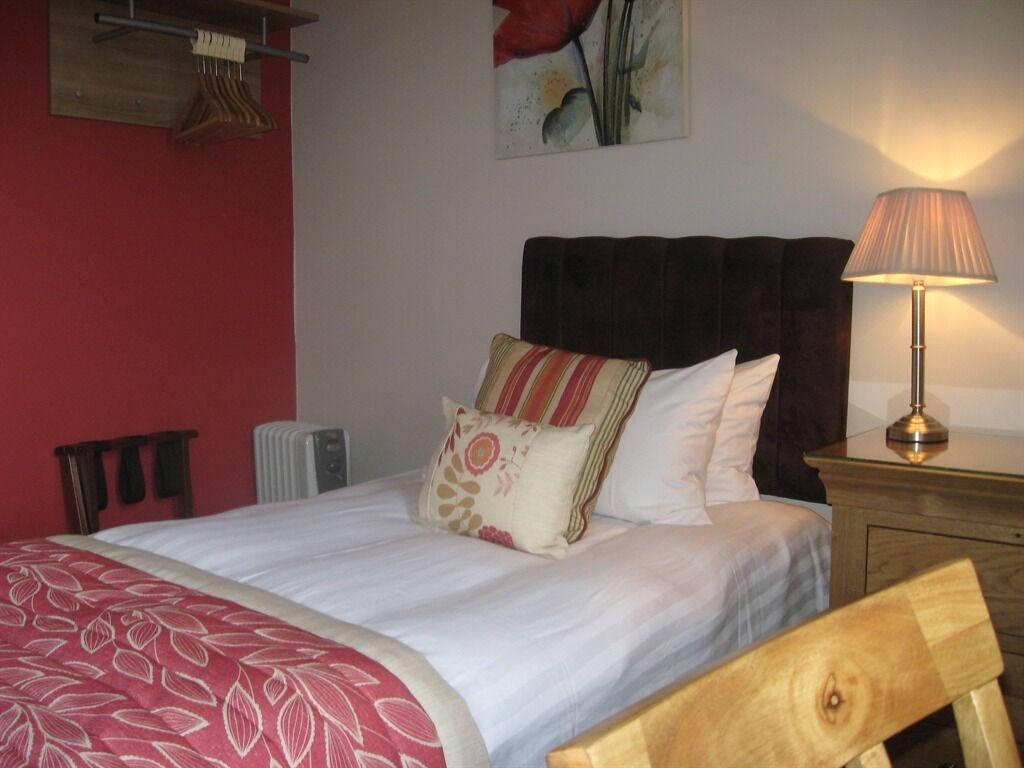 A neatly made bed with a patterned bedspread, a wooden headboard, and a bedside lamp.