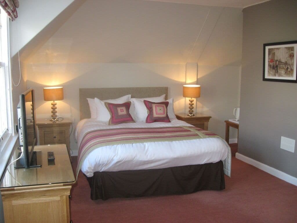 A bedroom with a bed, two bedside tables, lamps, a nightstand, a dresser, and a framed picture on the wall.