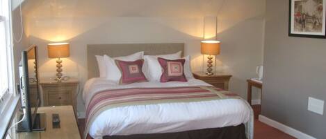 A bedroom with a bed, two bedside tables, lamps, a nightstand, a dresser, and a framed picture on the wall.