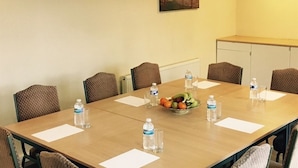 Ein Konferenzraum mit einem langen Tisch, Stühlen, Wasserflaschen und einer Obstschale.