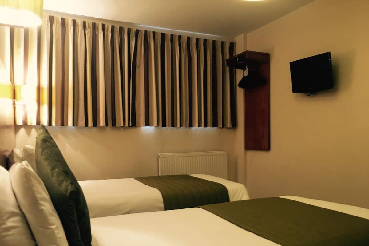 A hotel room with two beds, a television mounted on the wall, and a window with curtains.