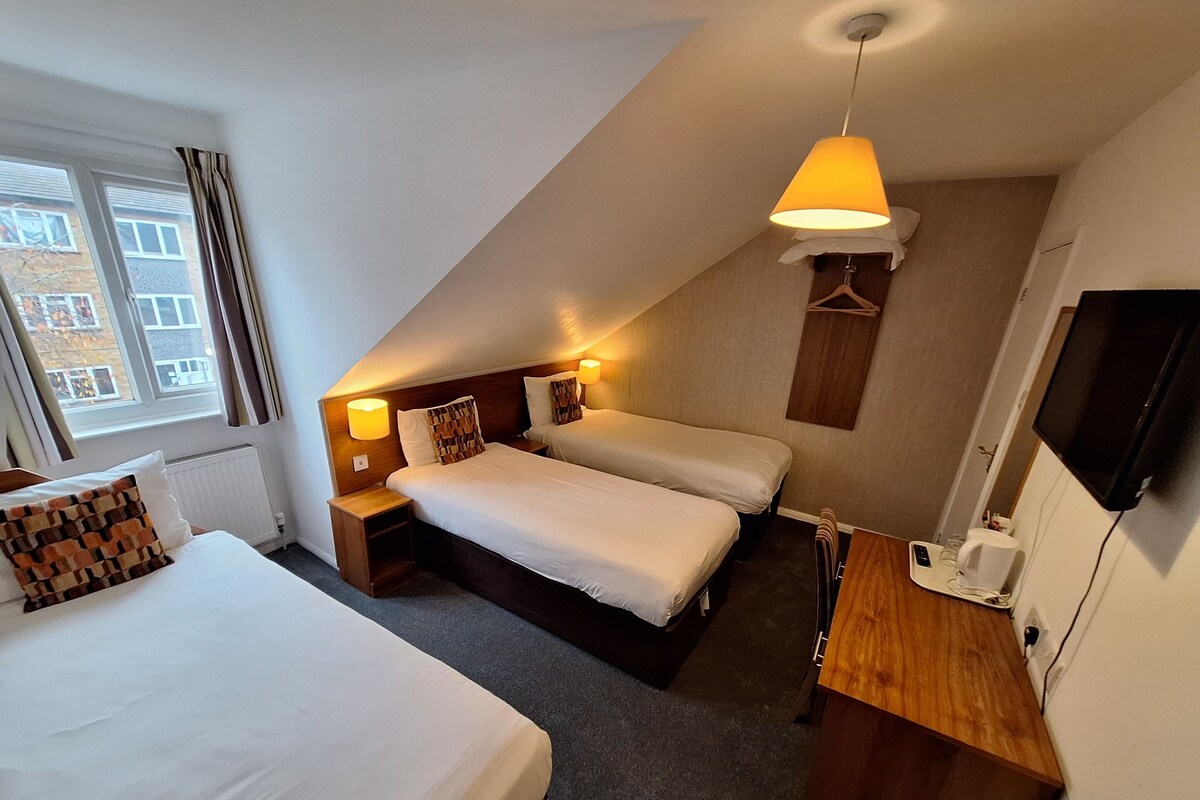 A hotel room with two beds, a desk, a TV, and a window with curtains.