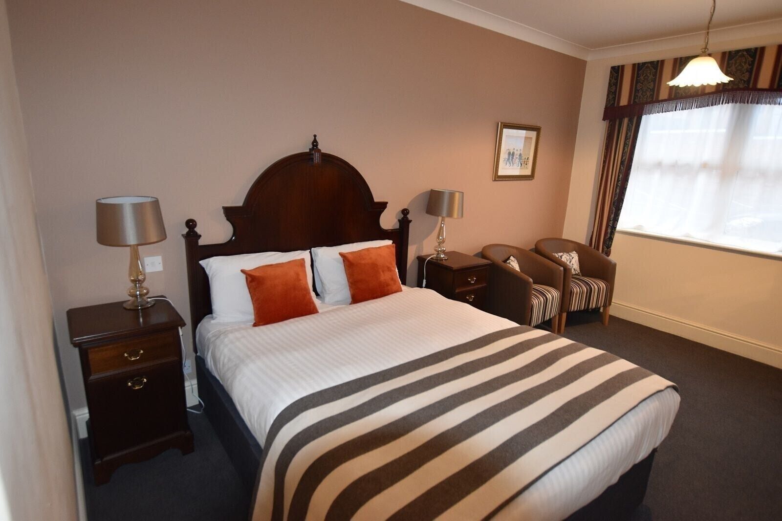 A neatly arranged hotel room with a large bed, two bedside tables, a chair, and a window with curtains.