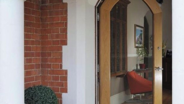Una puerta de madera con un panel de vidrio, columnas blancas y un muro de ladrillo.