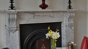Una habitación con chimenea, un cuadro enmarcado de un paisaje urbano, una bandeja con galletas y una taza, y un florero con flores.