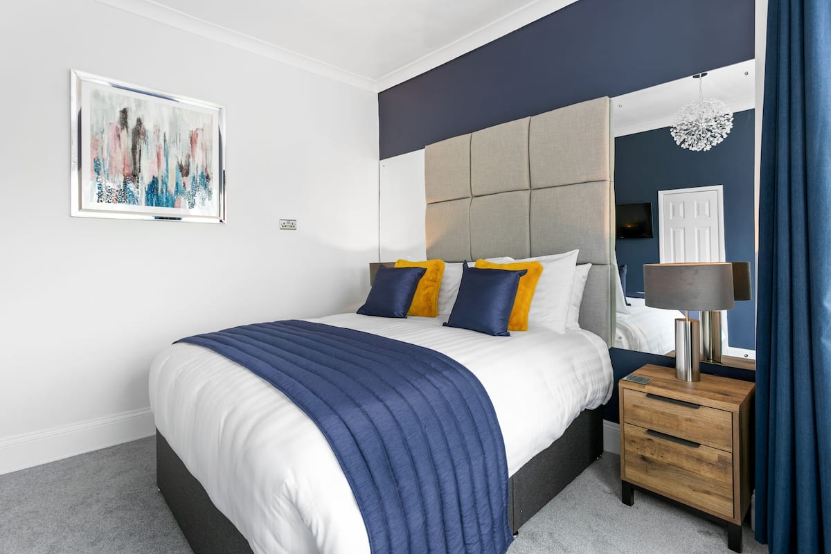 A modern bedroom with a large bed, a bedside table, a wall-mounted TV, and a decorative light fixture.