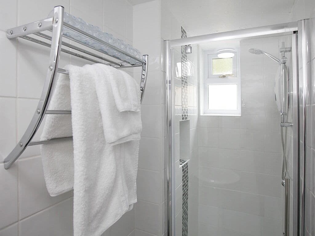 A bathroom with a glass shower enclosure, a chrome towel rack with white towels, and white tiled walls.