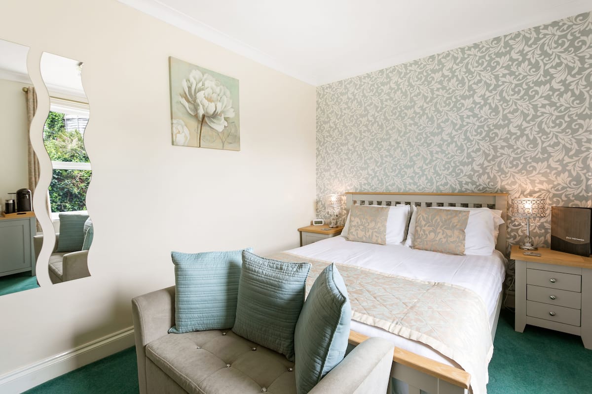A bedroom with a bed, a nightstand, a lamp, a mirror, and a chair.