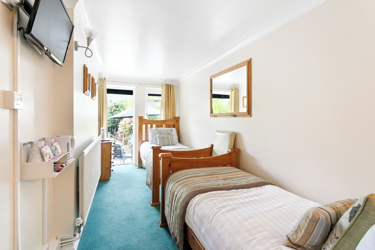 A bedroom with two single beds, a TV, a mirror, and a window with curtains.