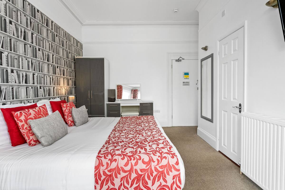A bedroom with a large bed, a bookshelf, a desk, and a wardrobe.