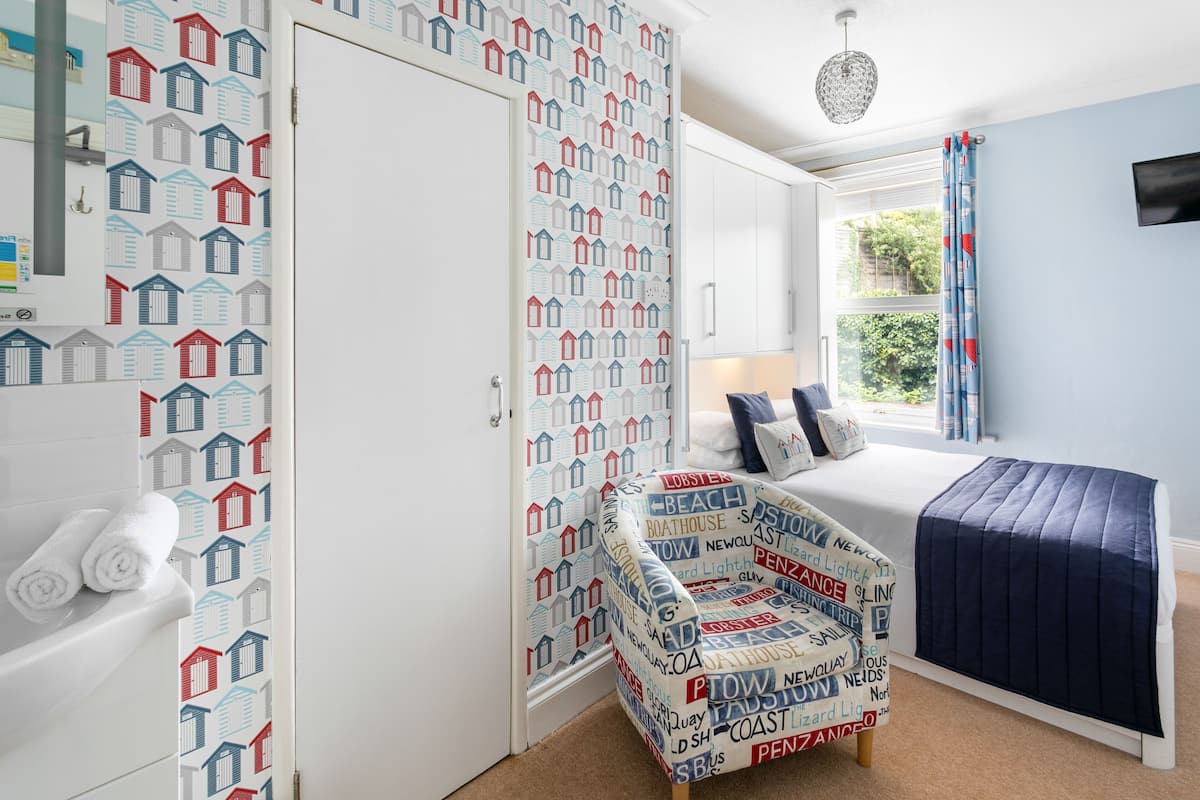 A bedroom with a bed, a chair, a window with curtains, and a wall with a house pattern.