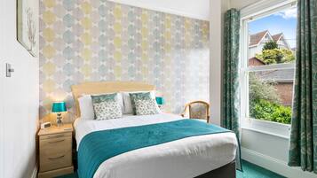 A bedroom with a bed, bedside tables, a window with curtains, and a patterned wall.