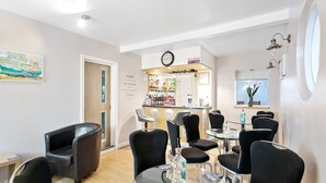 A hotel lobby with a bar area, black leather chairs, a round table with a clock, and a painting on the wall. - Mount Edgcombe Guest House (Torquay)