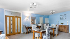 A dining area with a wooden table and chairs, a chandelier, and a clock on the wall. - Mount Edgcombe Guest House (Torquay)