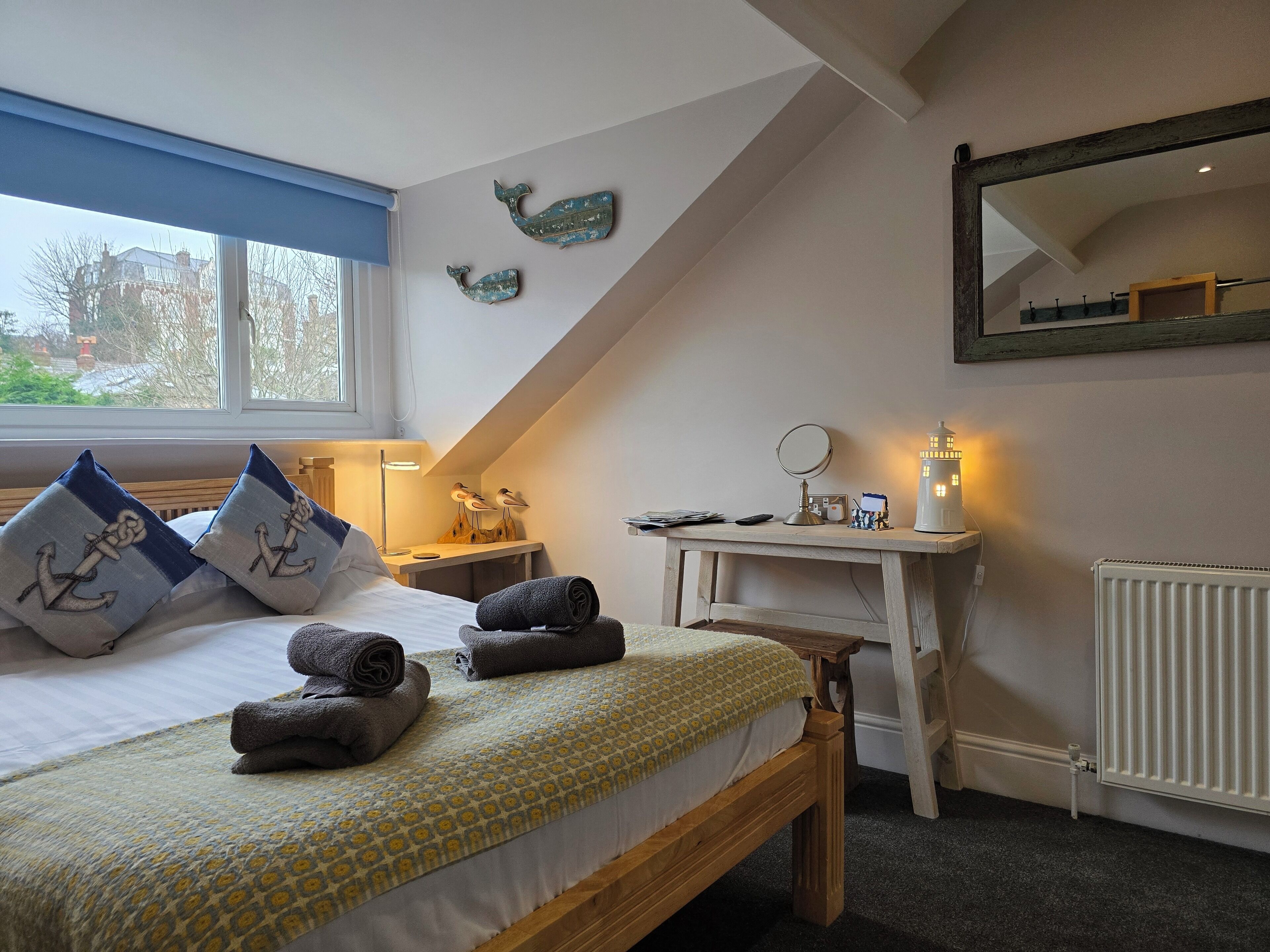 A bedroom with a bed, pillows, a bedside table with a lamp, a mirror, and a radiator.