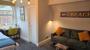 A cozy room with a green sofa, a small wooden stool, a desk with a chair, and a wall sign pointing to the beach. - Ashburton House (Scarborough)