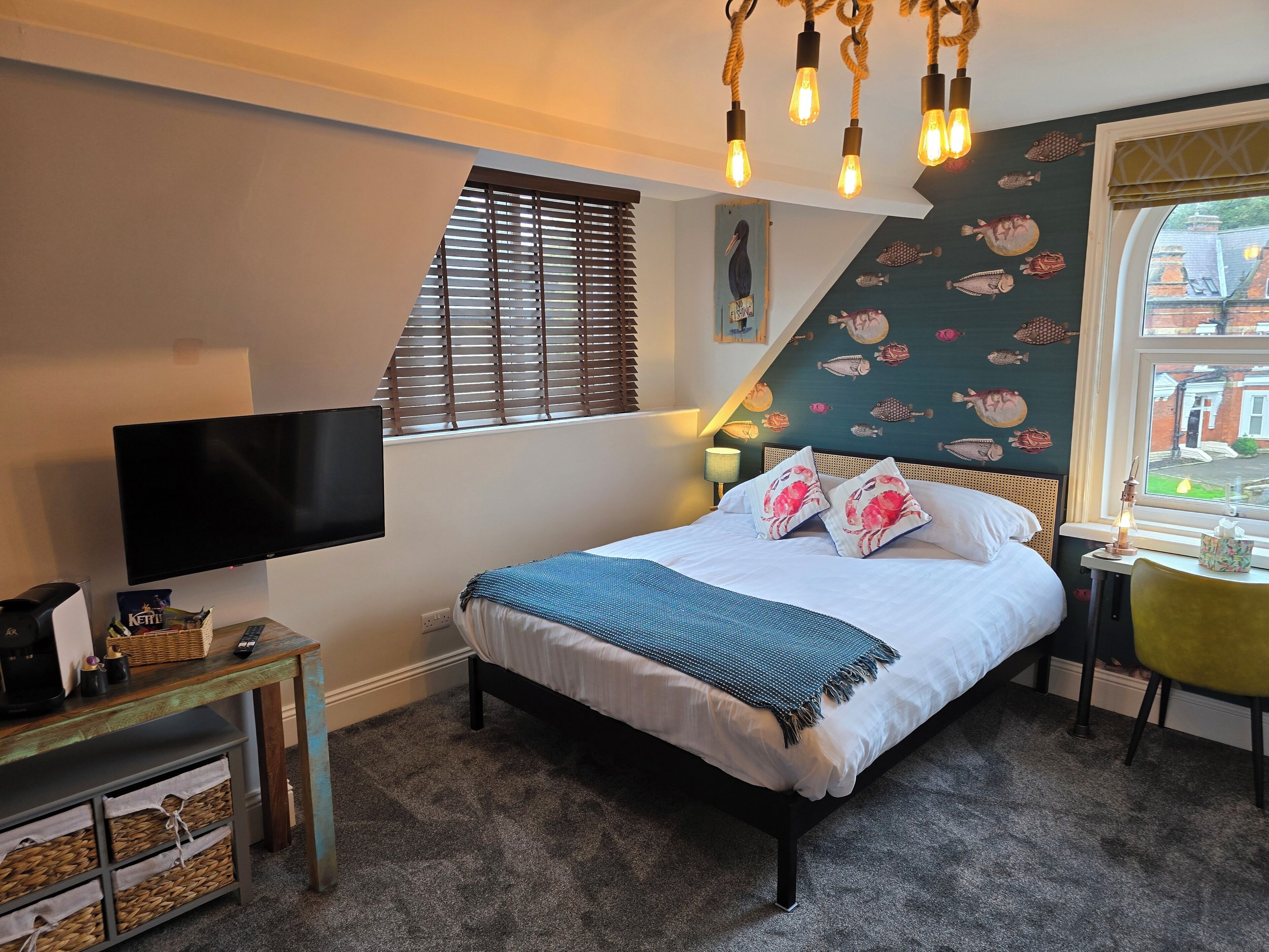 Een slaapkamer met een bed, een televisie, een bureau en een raam met jaloezieën.