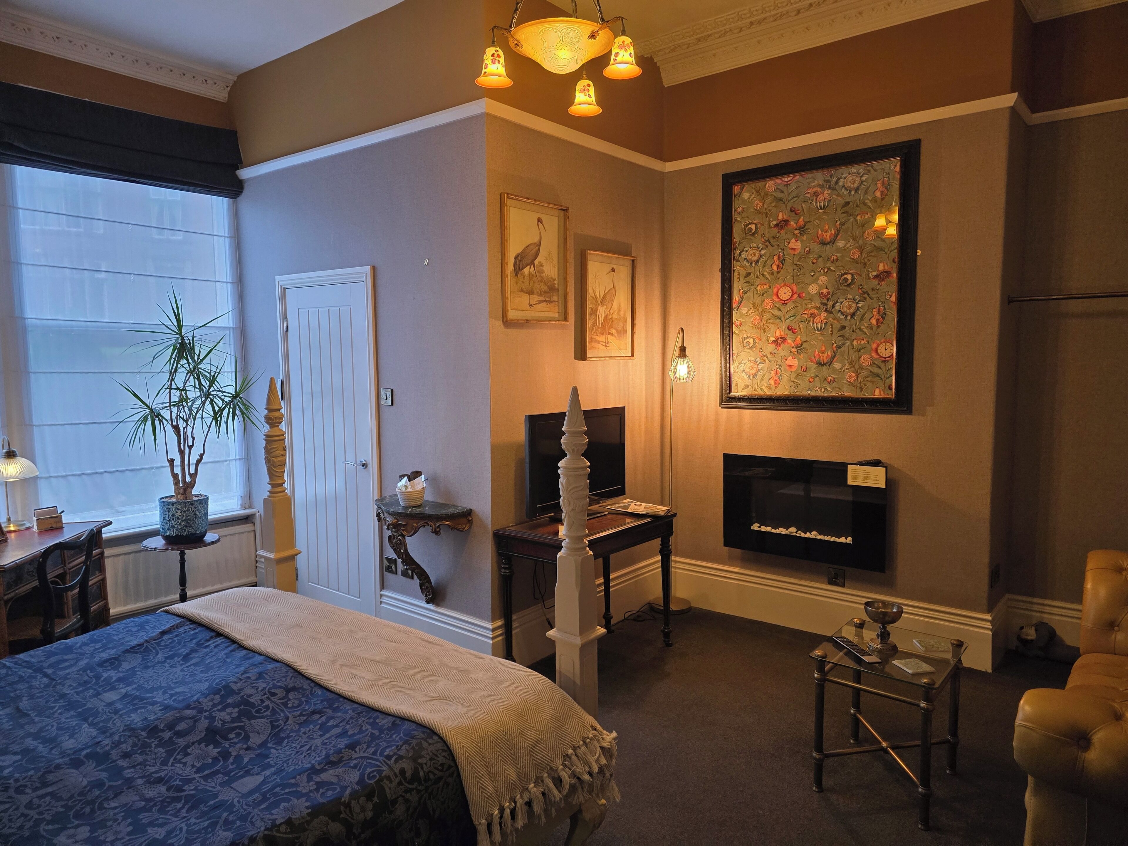 A bedroom with a bed, a desk, a television, and a fireplace.