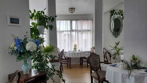 Comedor con mesa redonda, sillas y lámpara de araña. Hay plantas en macetas y un espejo en las paredes.