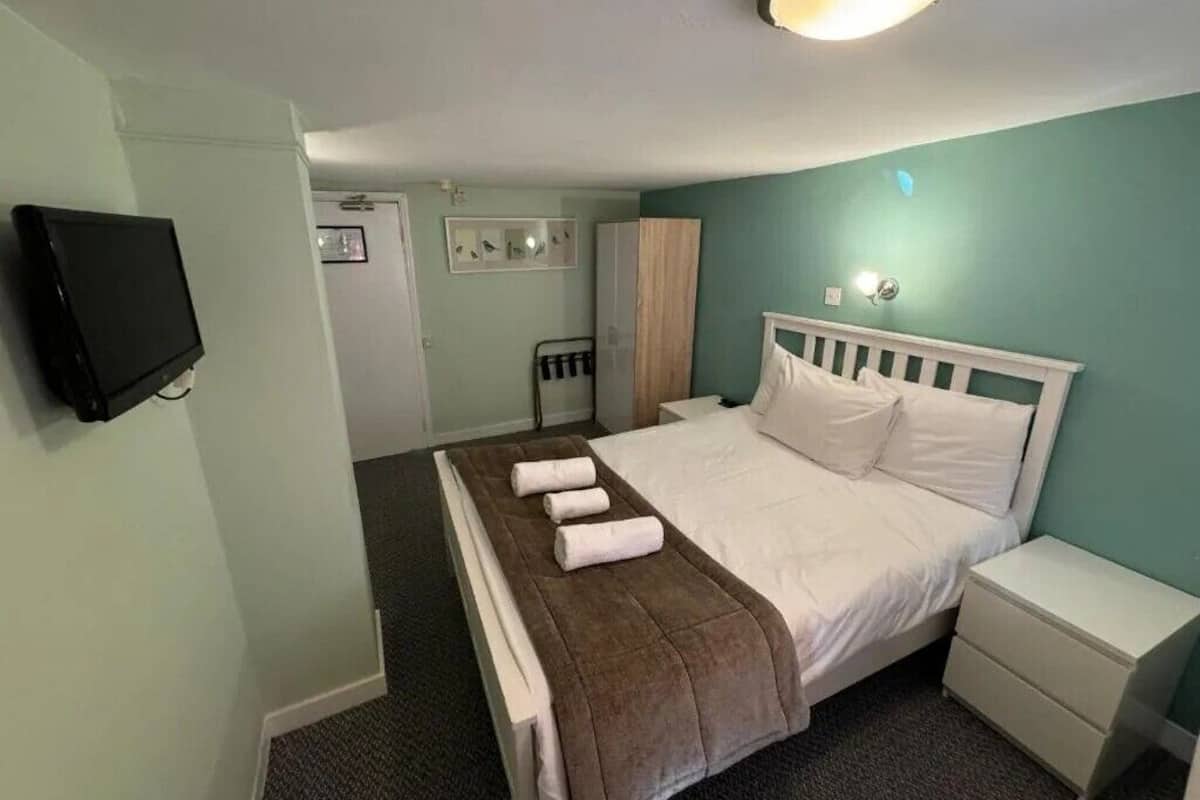 A hotel room with a bed, a bedside table, a TV, and a door.