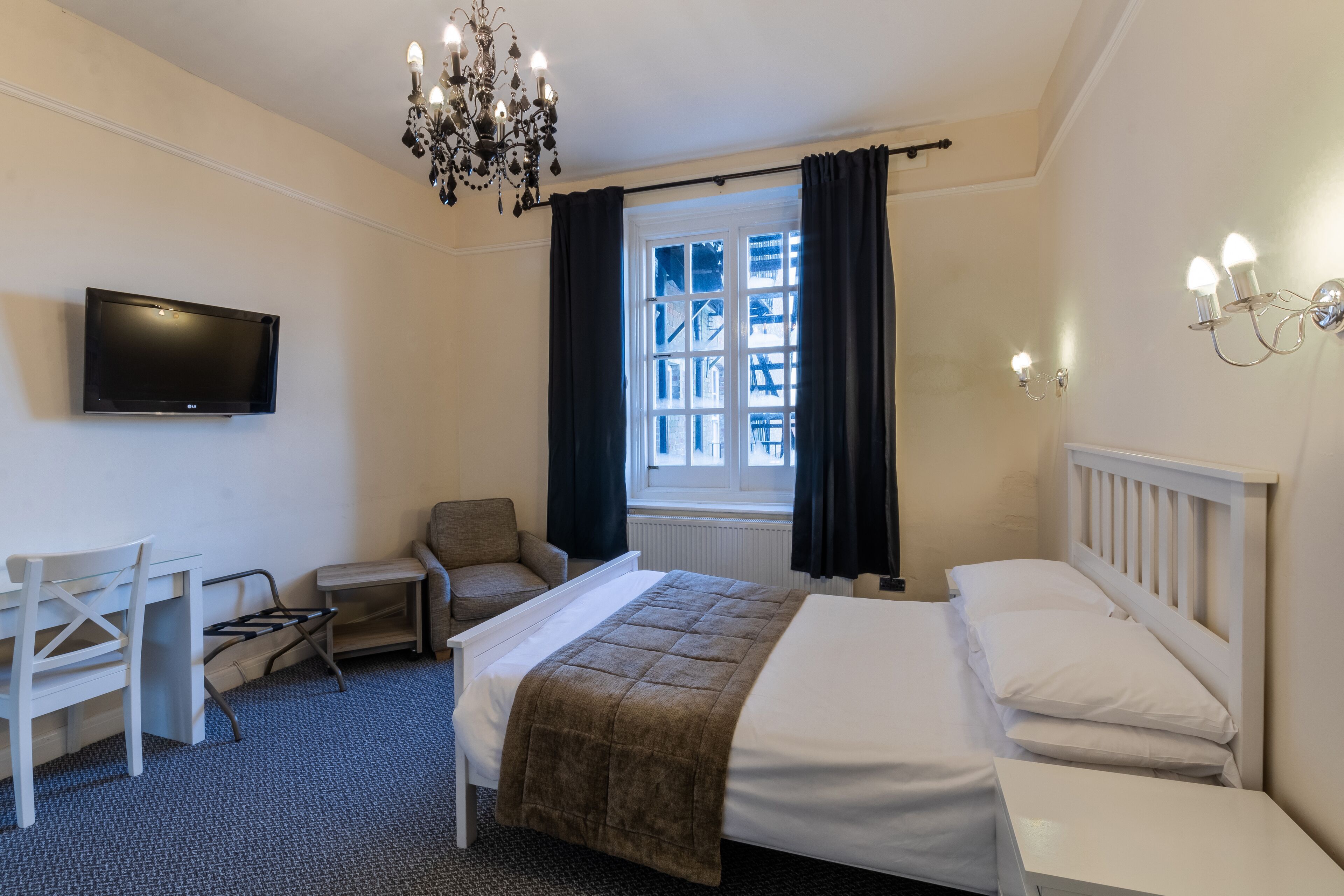Ett hotellrum med en säng, en stol, ett skrivbord, en tv och ett fönster med gardiner.