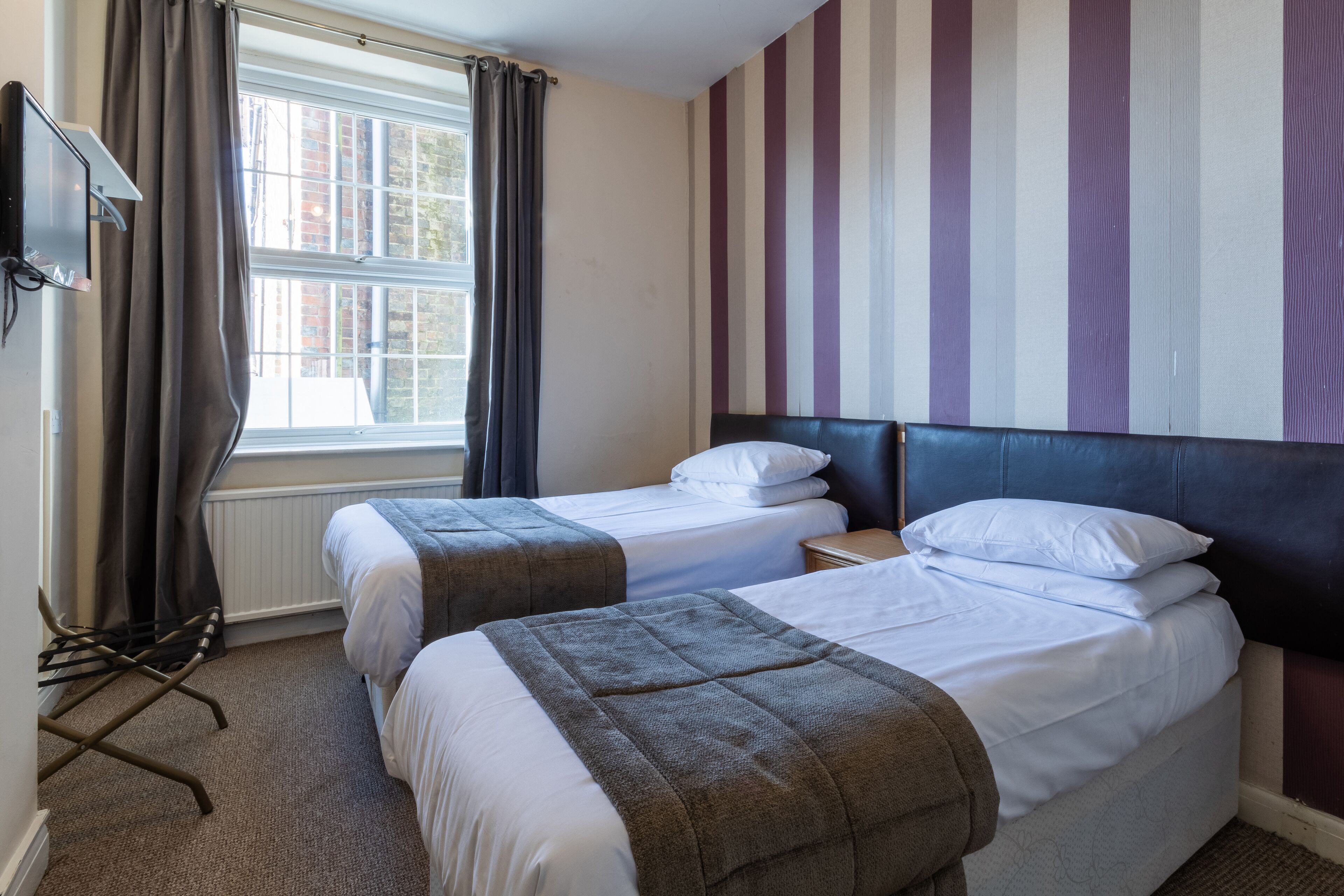 A hotel room with two beds, a TV, a window with curtains, and a striped wall.