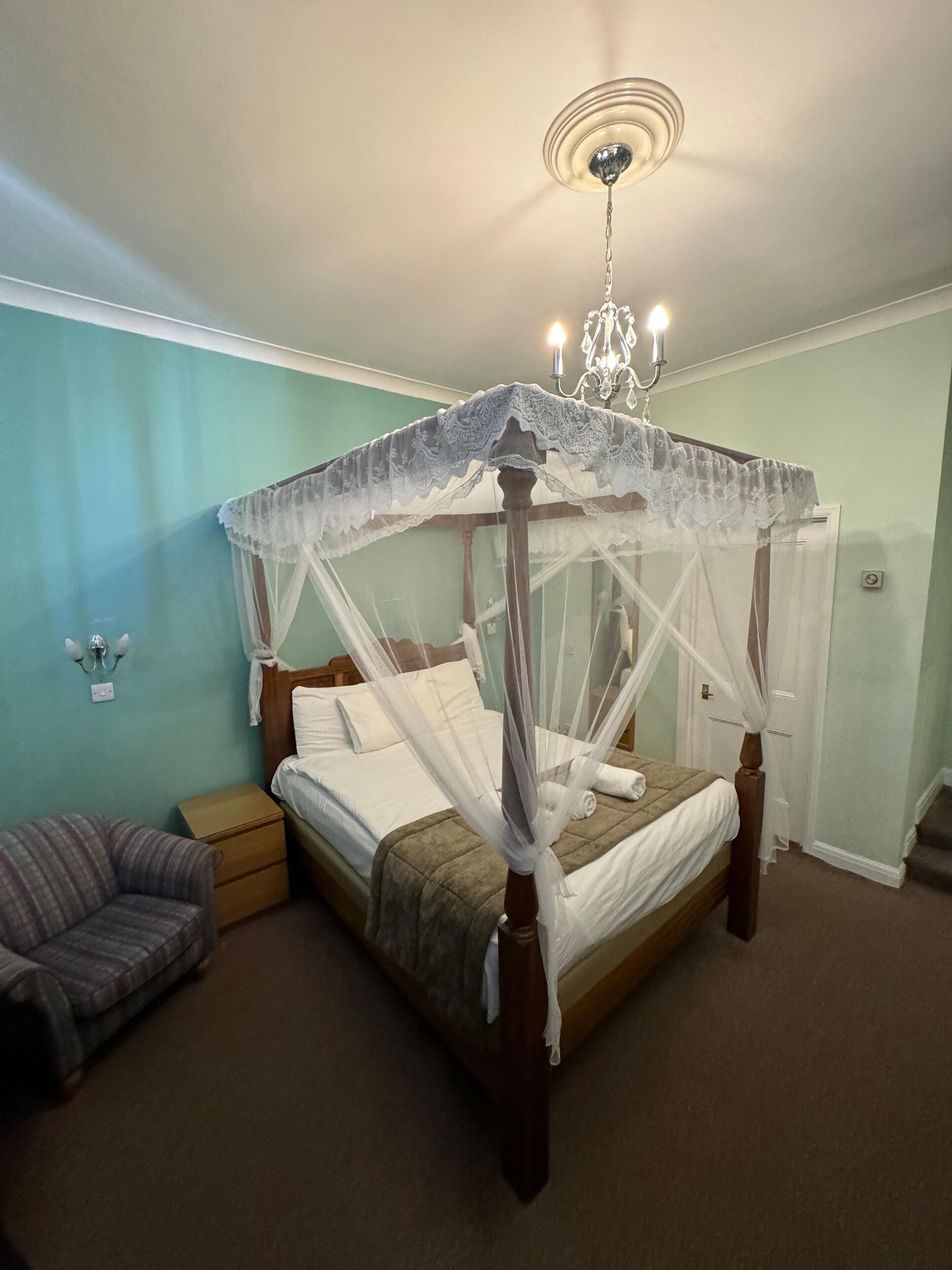 Ein Himmelbett mit Baldachin, eine Chandelier, ein Nachttisch und ein kleiner Stuhl.