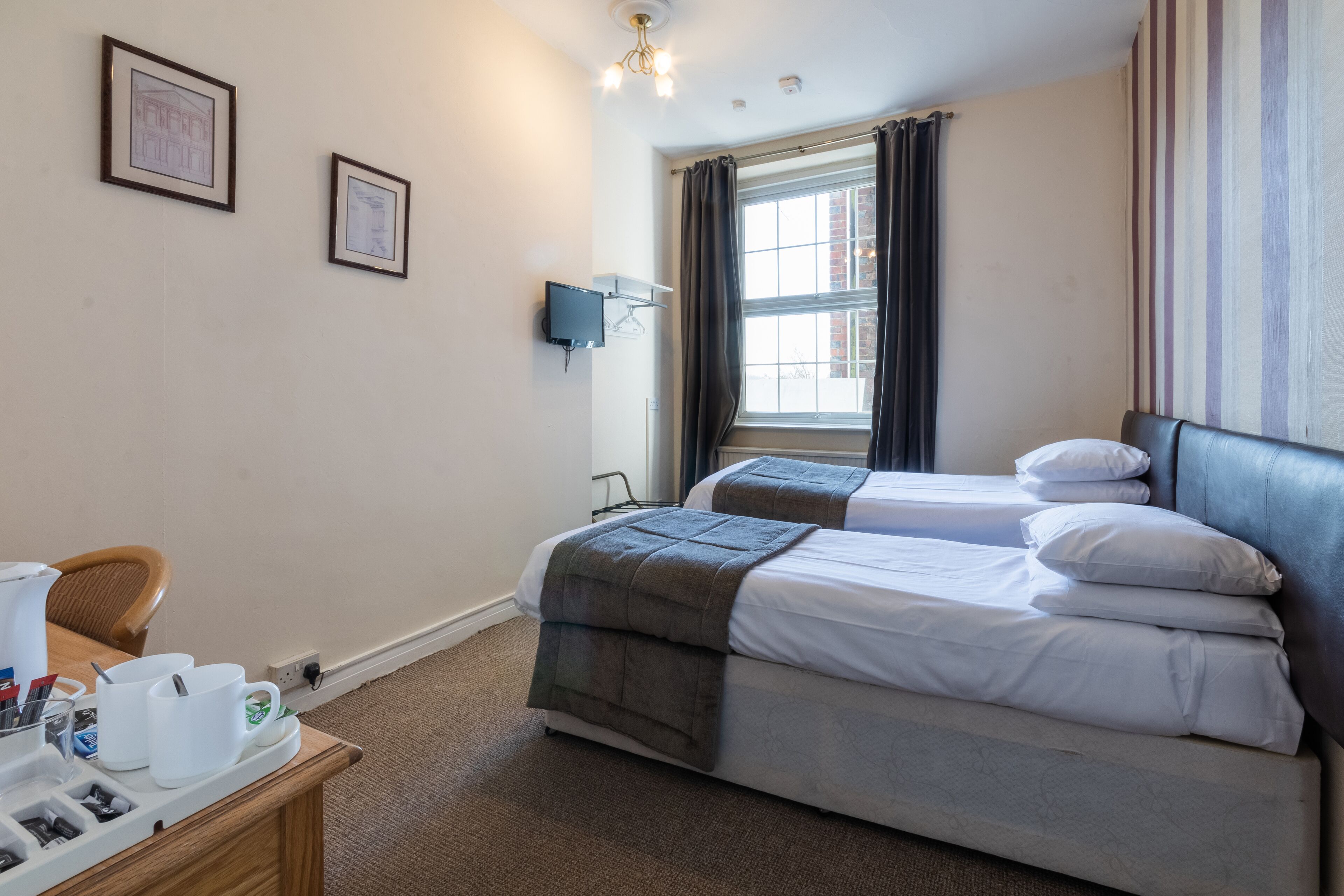 A hotel room with two beds, a desk with a coffee maker, and a window with curtains.