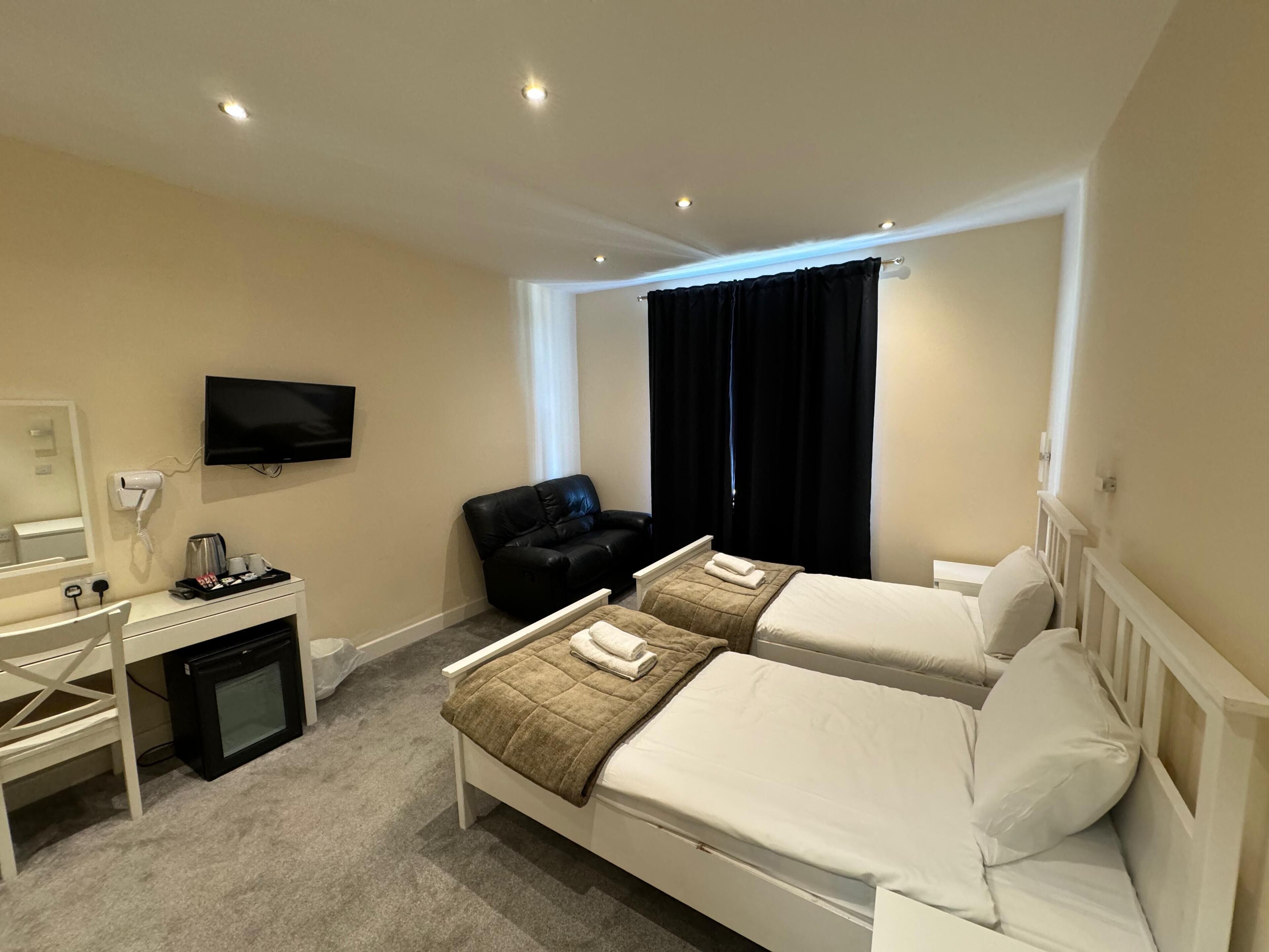 A hotel room with two beds, a desk with a hairdryer, a TV, and a window with curtains.