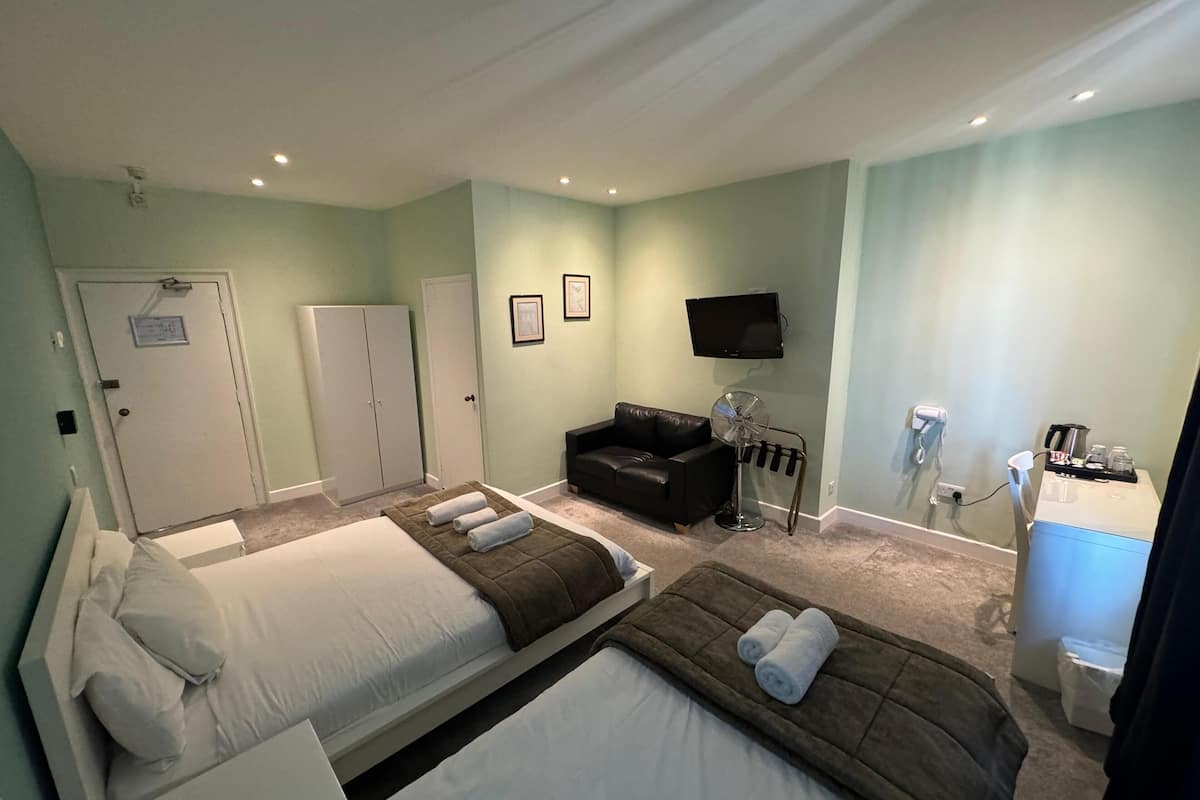 A hotel room with two beds, a sofa, a TV, and a desk with a phone and a coffee machine.