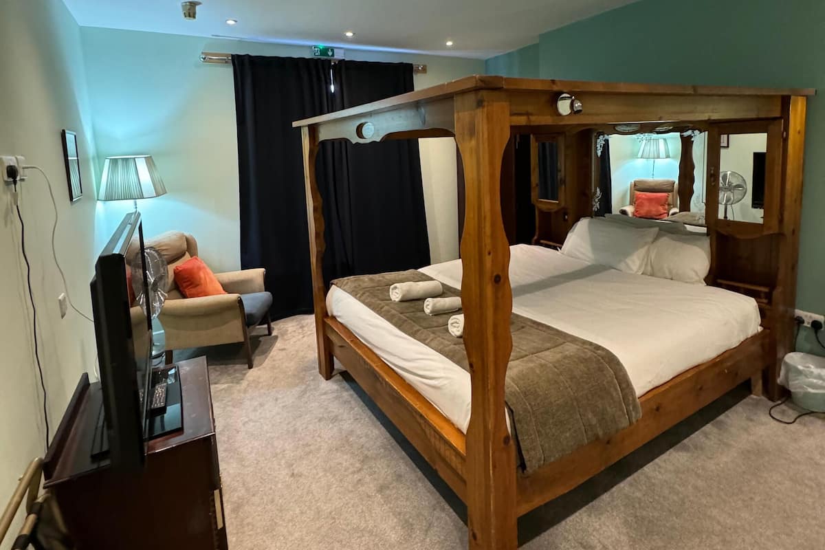 A four-poster bed with a wooden frame, a flat-screen TV on a stand, a sofa with cushions, and a lamp.