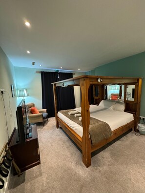 A four-poster bed with a wooden frame, a flat-screen TV on a stand, a sofa with cushions, and a lamp.