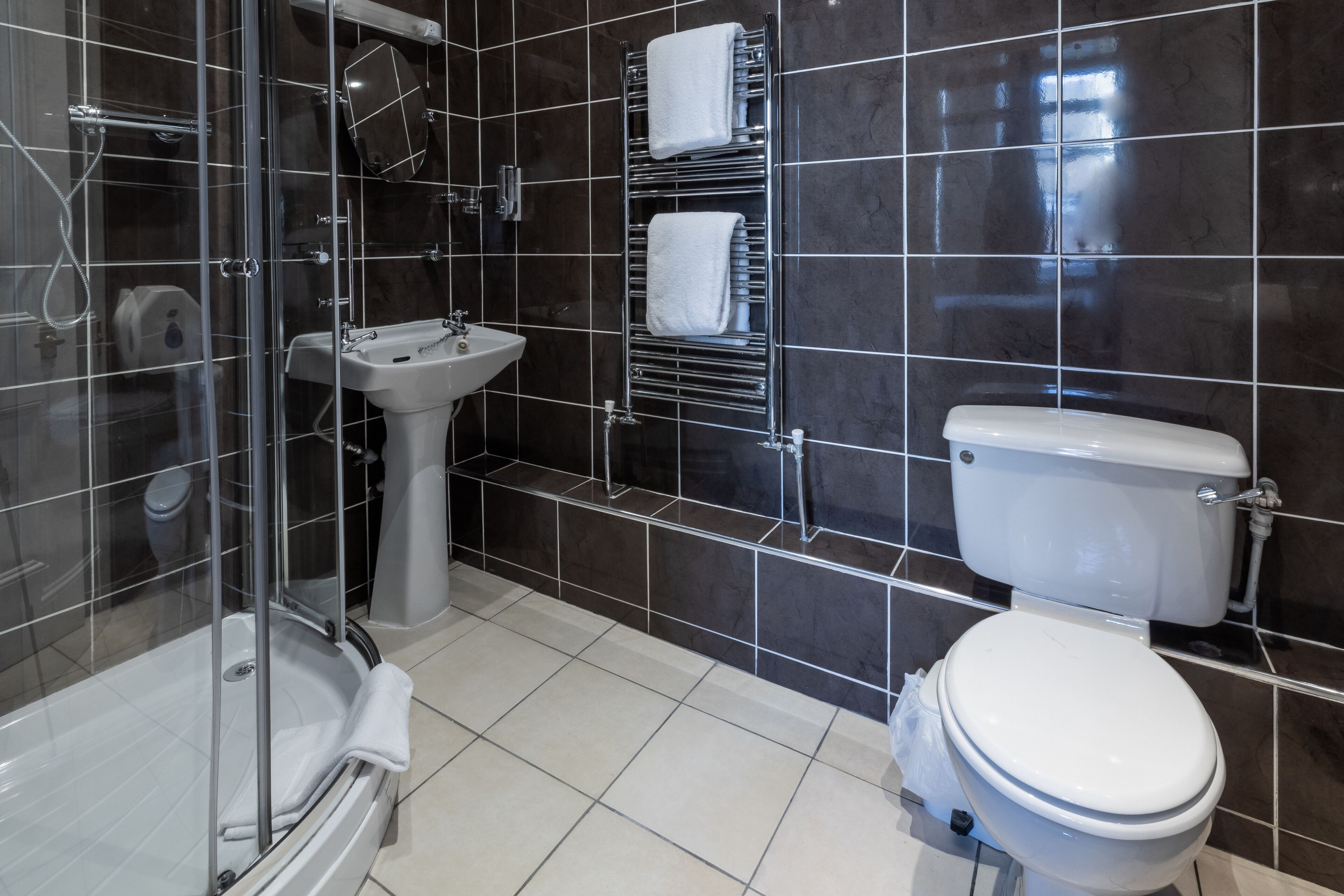A modern bathroom with a glass-enclosed shower, a pedestal sink, and a toilet.