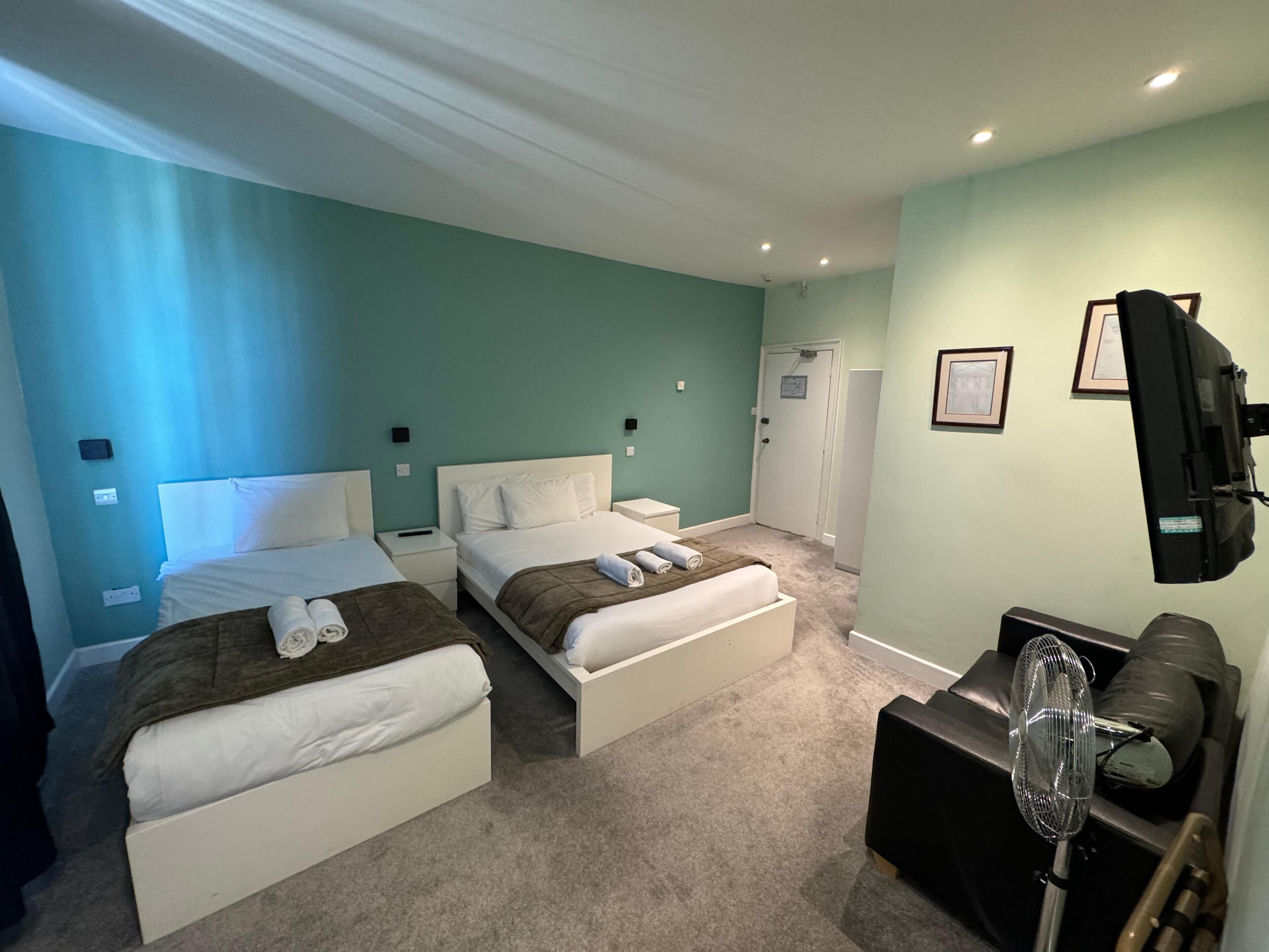 A hotel room with two beds, a TV, a fan, and a door leading to a bathroom.