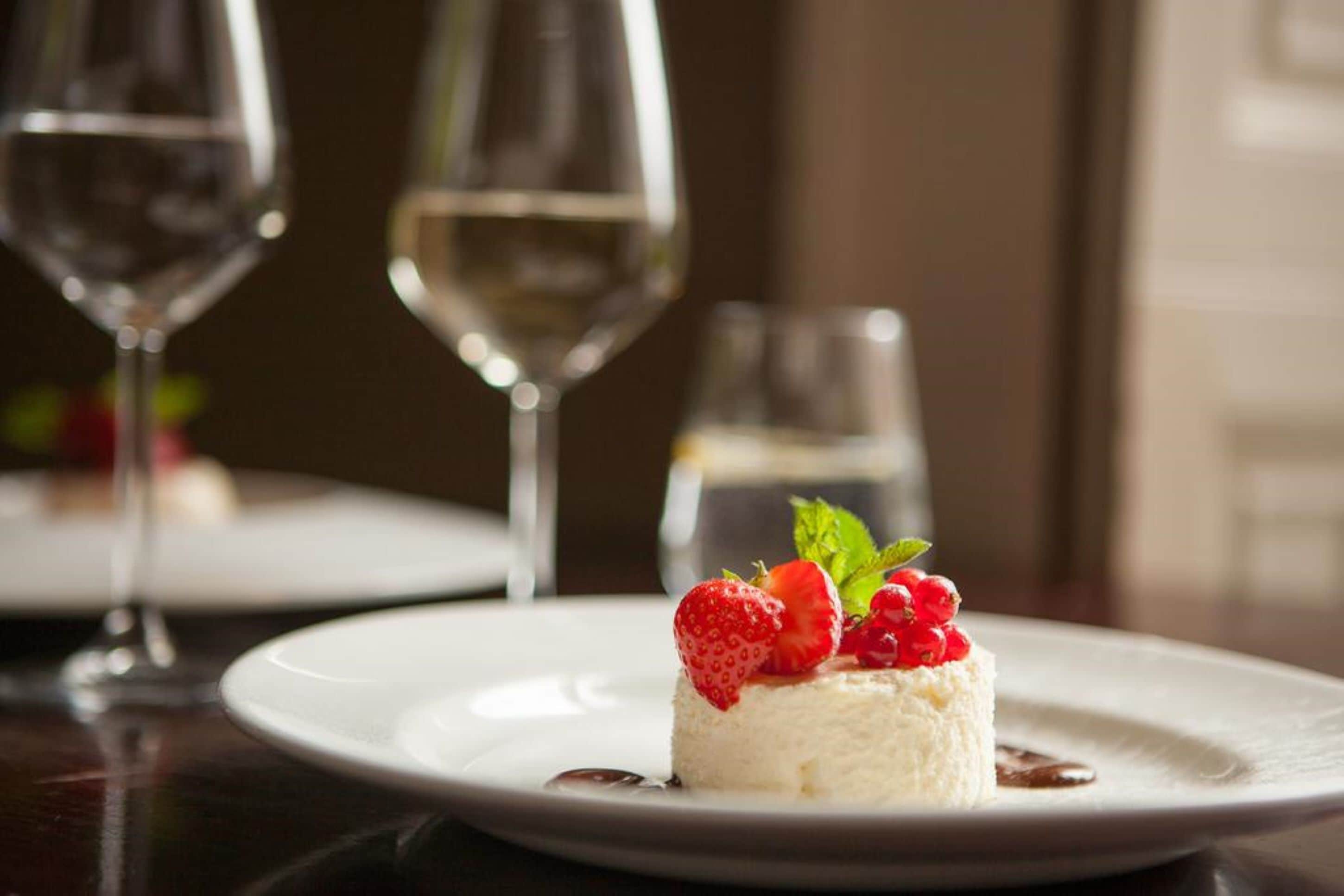 A dessert on a white plate with strawberries and berries, accompanied by a glass of white wine and a water glass.