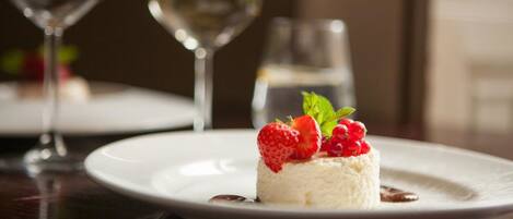 A dessert on a white plate with strawberries and berries, accompanied by a glass of white wine and a water glass.