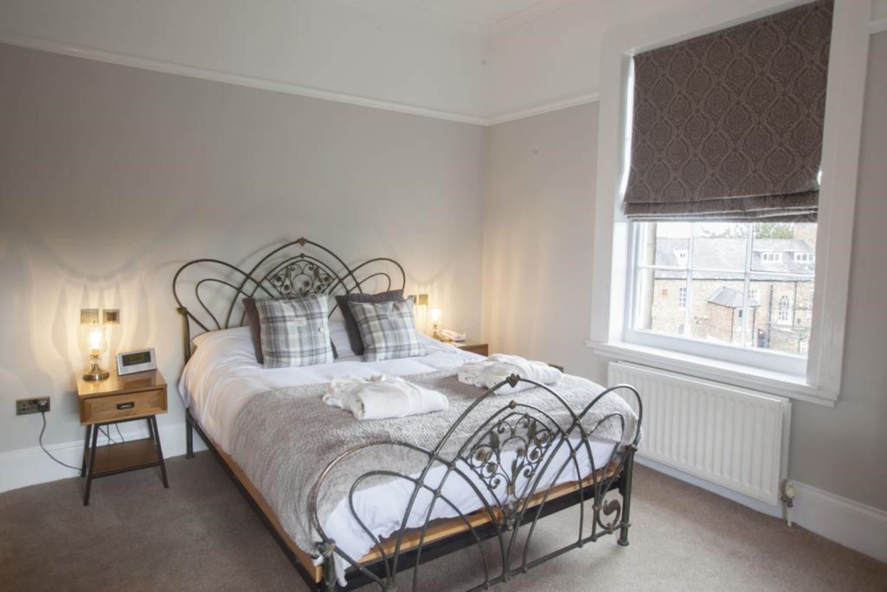 A neatly made bed with a metal frame, two bedside tables with lamps, and a window with a patterned blind.