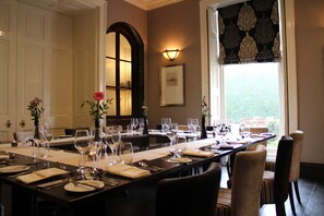 A dining area with a long table set for a meal, chairs, and a window with a view.