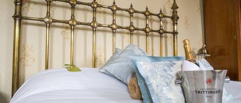 A bed with a metal headboard, a pillow, a blanket, and a bucket of champagne.