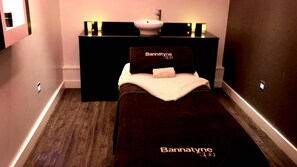 A small, dark-themed bedroom with a bed, a bedside table, a vanity with a mirror, and a sink.